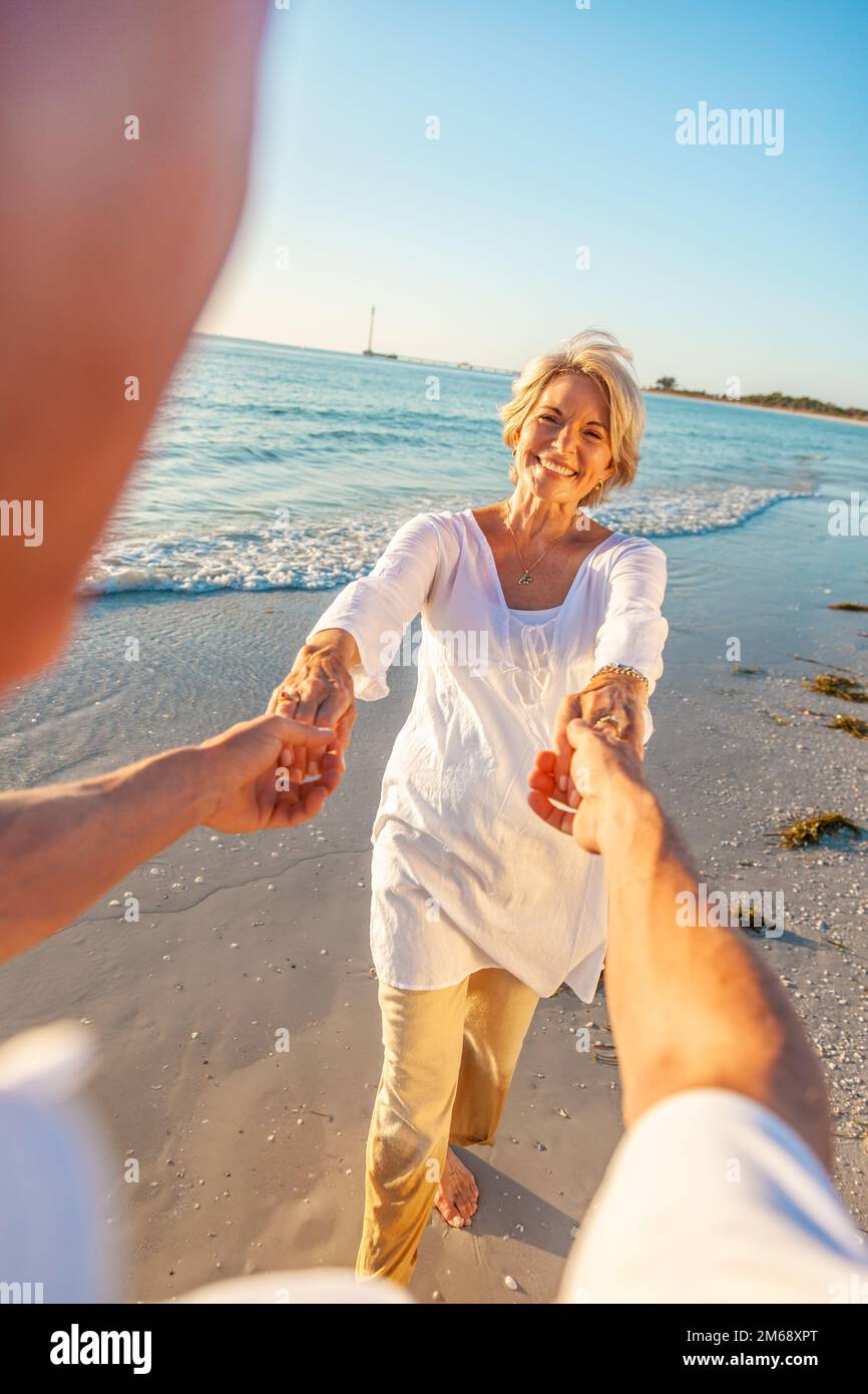 Un vieil homme et une femme retraités heureux dansent et tiennent la main sur une plage tropicale déserte avec un ciel bleu clair et lumineux Banque D'Images