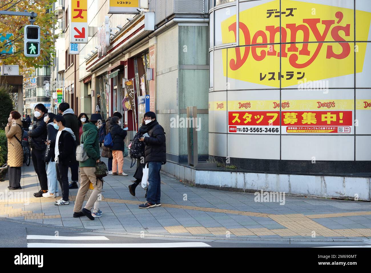 TOKYO, JAPON - 29 décembre 2022 : les gens attendent à un passage en croix au coin de la rue avec un restaurant Denny's dans la région de Tsukiji à Tokyo, lors d'une journée ensoleillée Banque D'Images