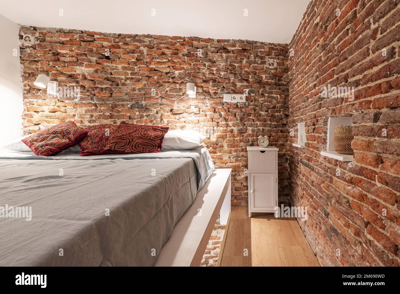 Chambre d'un loft en briques apparentes avec lit double avec coussins rouges et table de chevet en bois blanc Banque D'Images