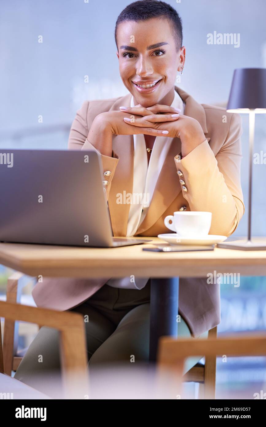 Une femme d'affaires décontractée et amicale aux cheveux courts est assise dans une cafétéria et sourit à la caméra. Il y a un ordinateur portable sur une table. Banque D'Images