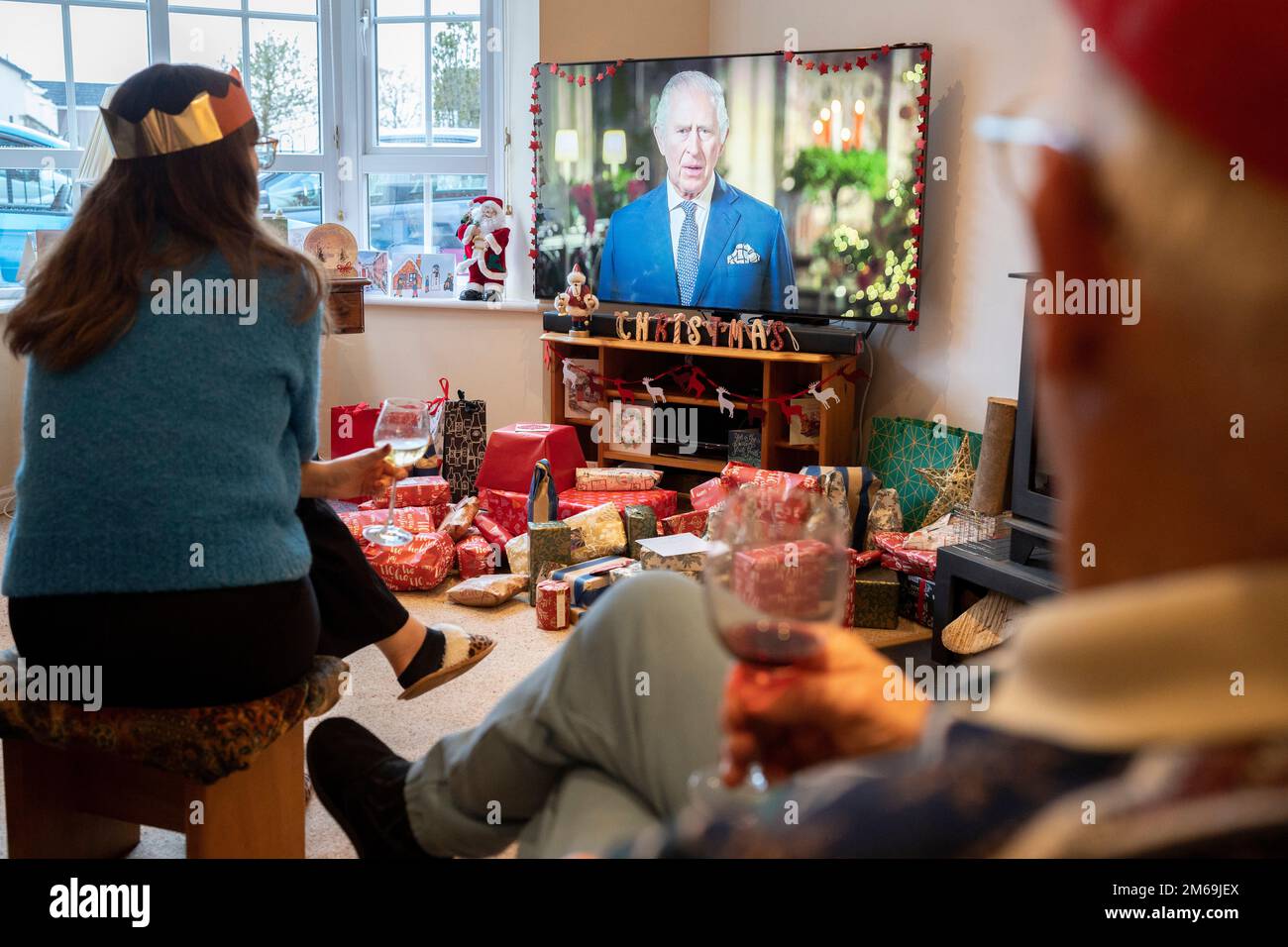 Lors de sa première émission du jour de Noël au pays depuis la mort de sa mère, la reine Elizabeth III en septembre, le roi Charles III parle à une famille de banlieue sur leur téléviseur grand écran dans leur salon rempli de cadeaux enveloppés, le 25th décembre 2022, à Nailsea, en Angleterre. Banque D'Images