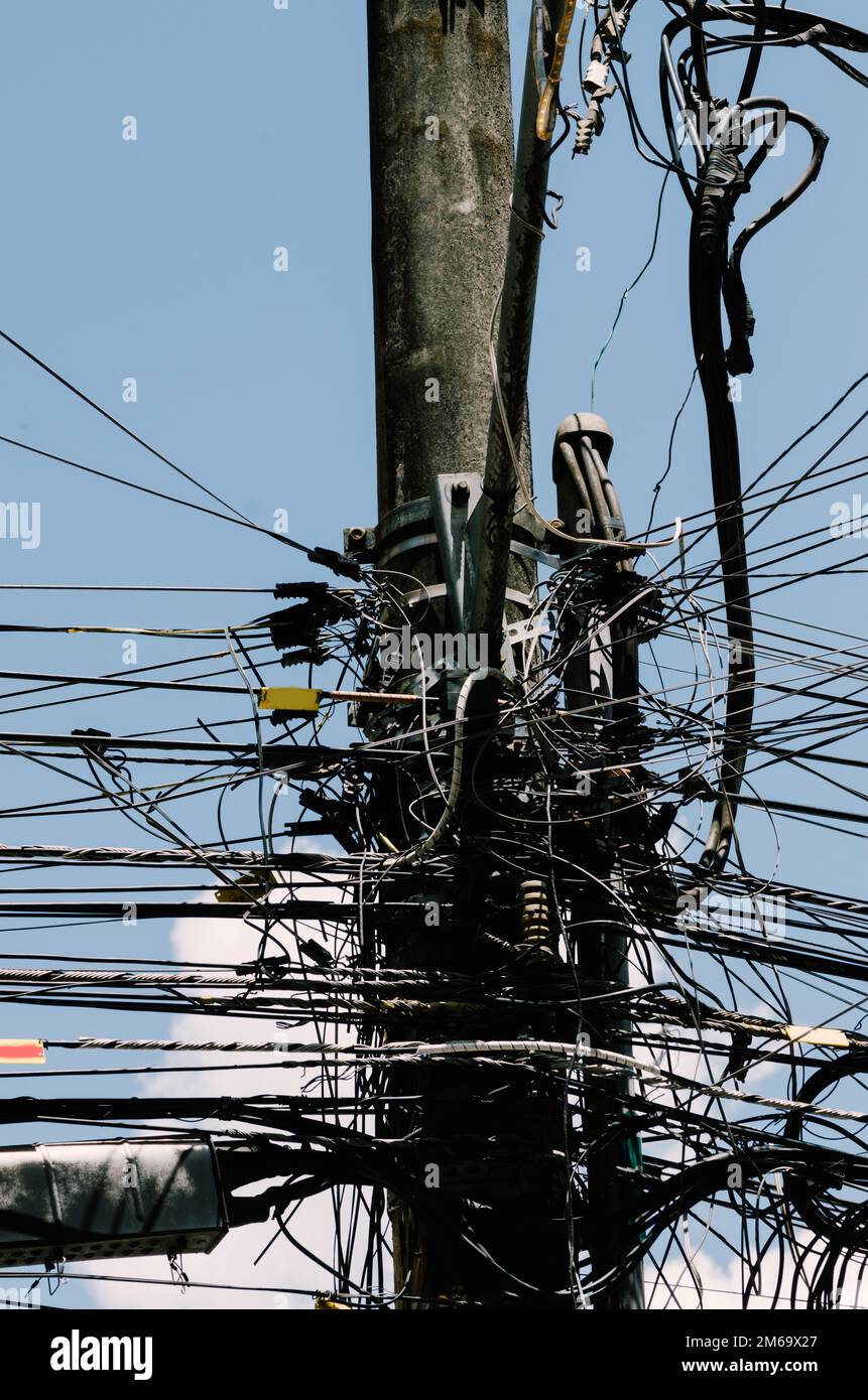 Beaucoup de fils attachés au poteau électrique, le chaos des câbles et des fils sur un poteau électrique, fond bleu ciel, concept de combinaison technologique Banque D'Images