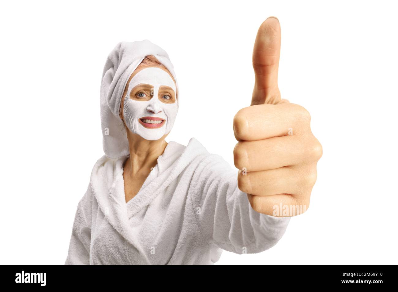 Femme dans un peignoir avec un masque de visage gestant les pouces vers le haut isolé sur fond blanc Banque D'Images