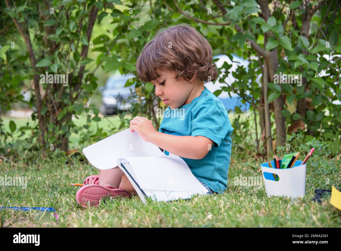 Enfant de l'école primaire couché sur l'herbe faisant les devoirs. Banque D'Images
