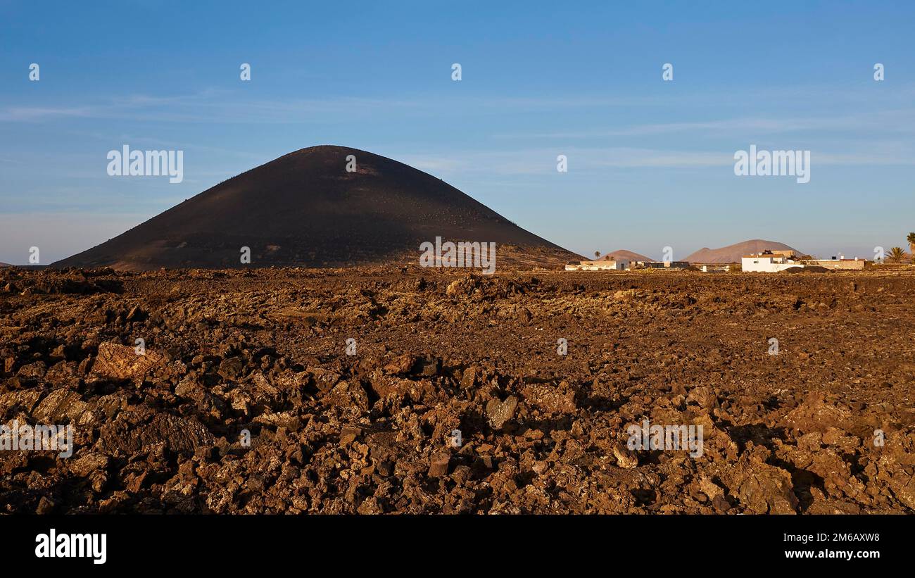 Champs de lave bruns, colline de lave noire, bâtiments bas, la Geria, région viticole, cave de vinification, El Grifo, musée du vin, ciel bleu, nuages blancs, Lanzarote Banque D'Images
