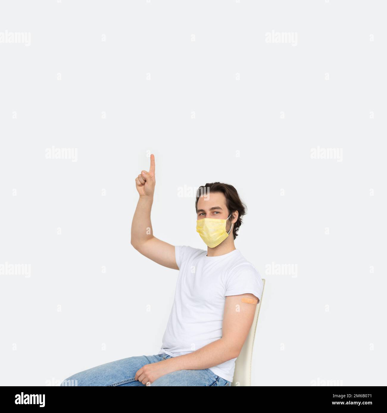 Un jeune homme de race blanche en masque de protection avec un aide-bracelet sur son épaule après la vaccination montre le doigt vers le haut sur l'espace vide Banque D'Images
