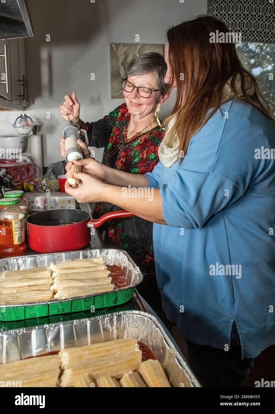 Deux femmes travaillent ensemble pour remplir les coquilles de pâtes de manucotti d'un mélange de fromage pour un plat de manucotti et de sauce marinara pour le dîner de la veille de Noël. Banque D'Images