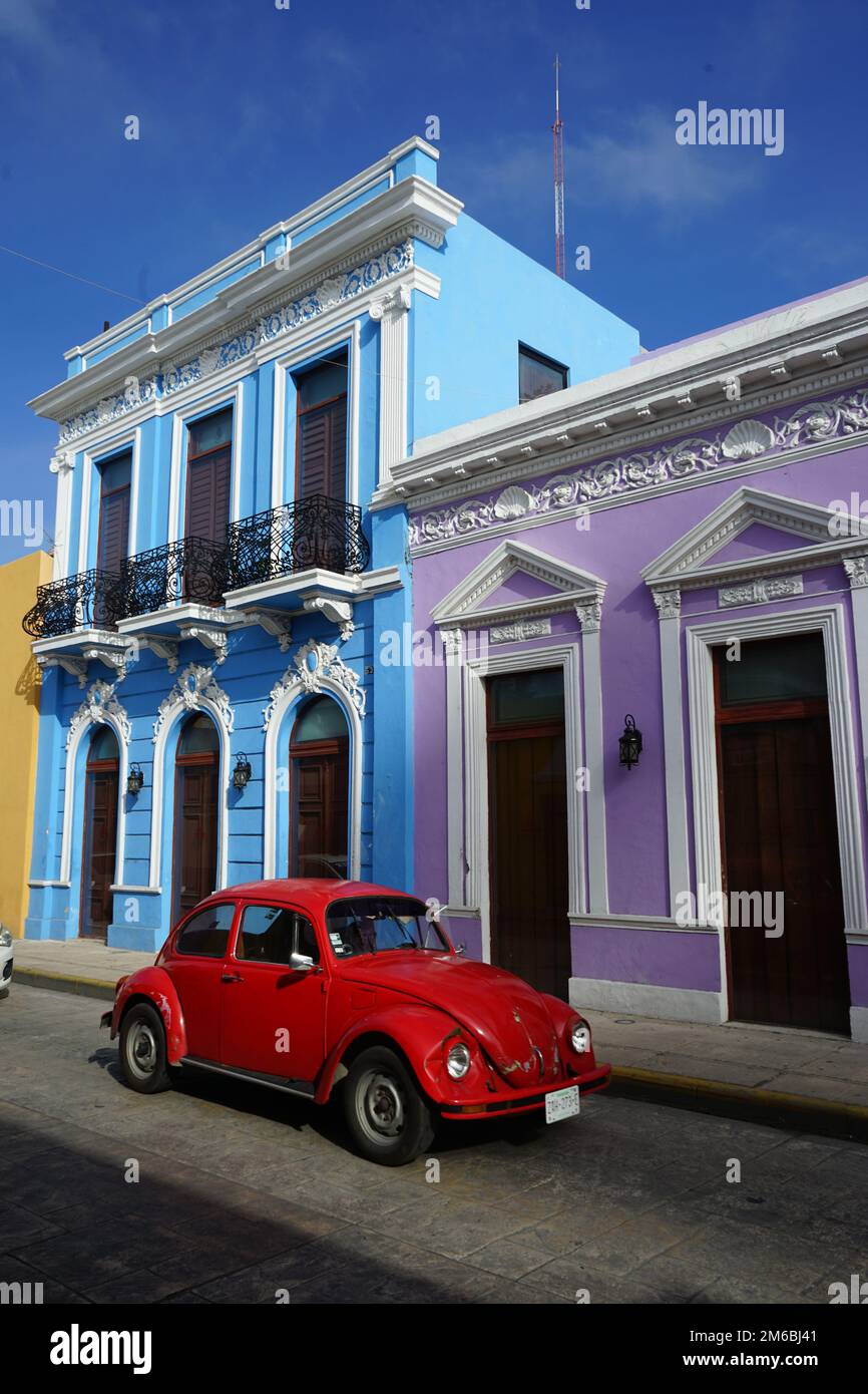 Une Volkswagen Beetle rouge vif passe devant des maisons du patrimoine violet et bleu restaurées sur la Calle 59, une rue célèbre de Merida Centro, Yucatan, Mexique Banque D'Images