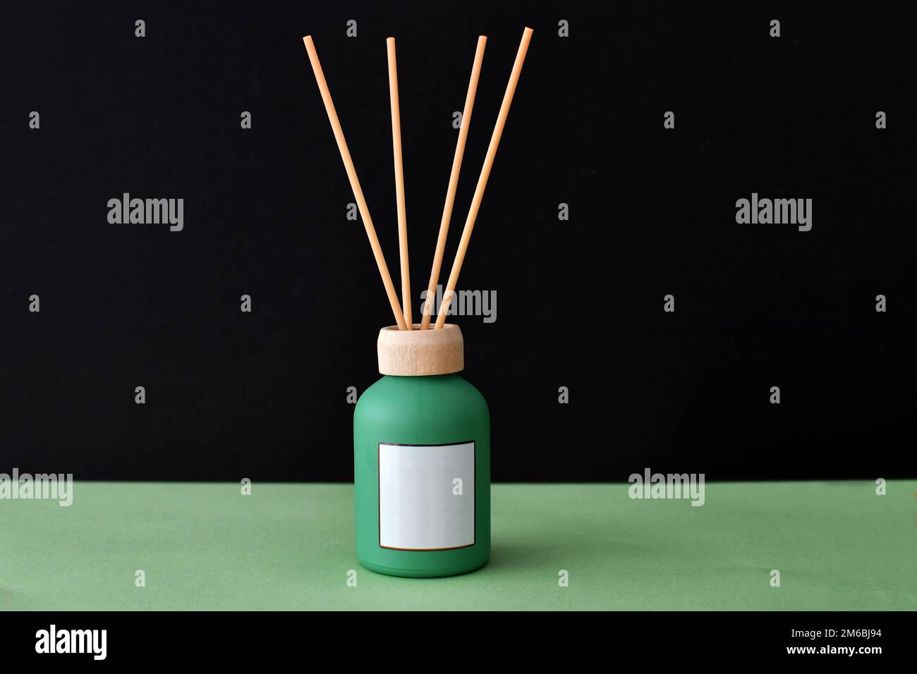 Flacon d'huile à diffuseur Reed avec étiquette blanche vierge sur une base verte isolée sur fond noir. Copier l'espace. Personne. Banque D'Images