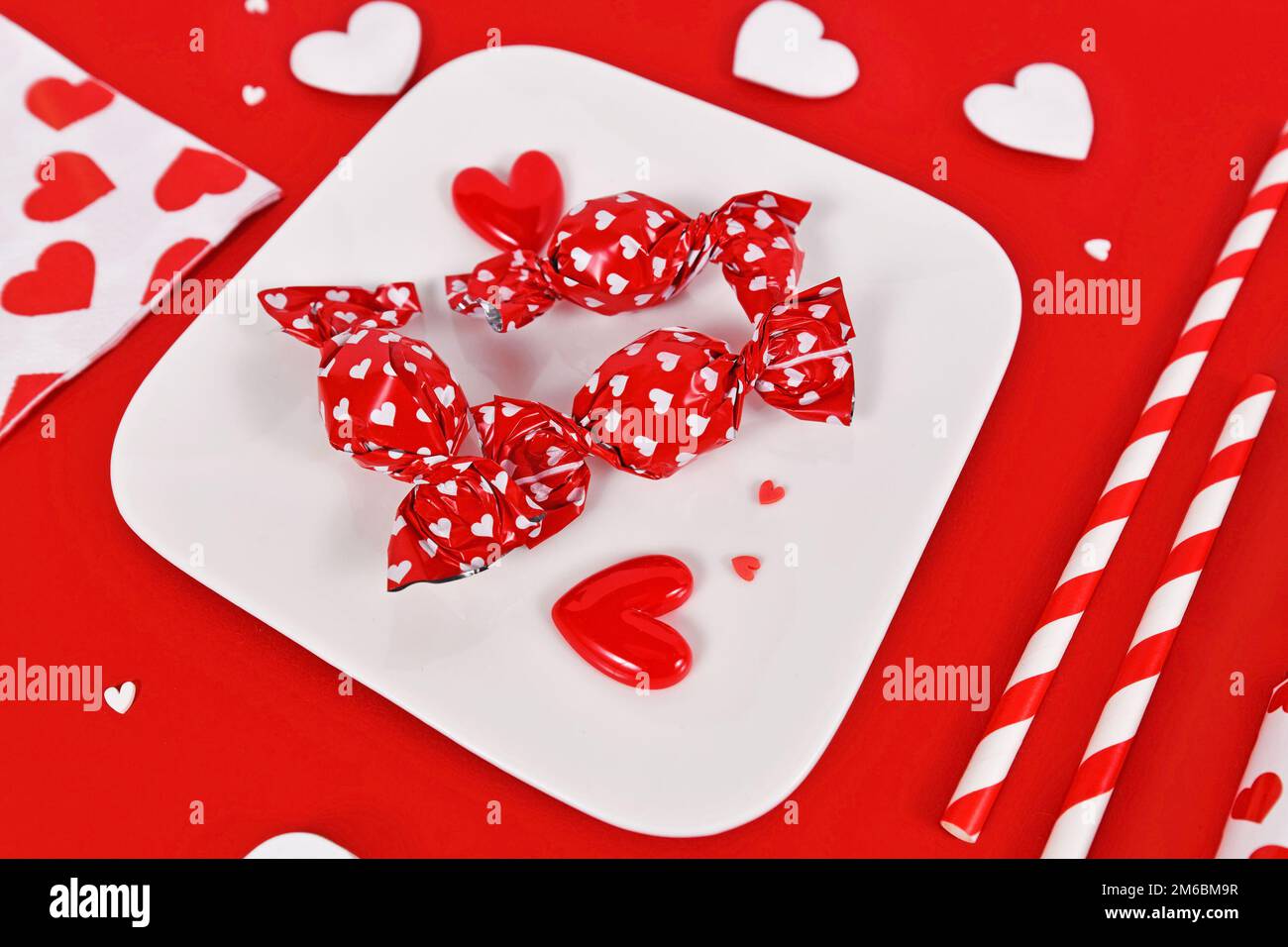 Friandises rouges de la Saint-Valentin avec emballage avec coeurs sur l'assiette entourée de décorations saisonnières Banque D'Images