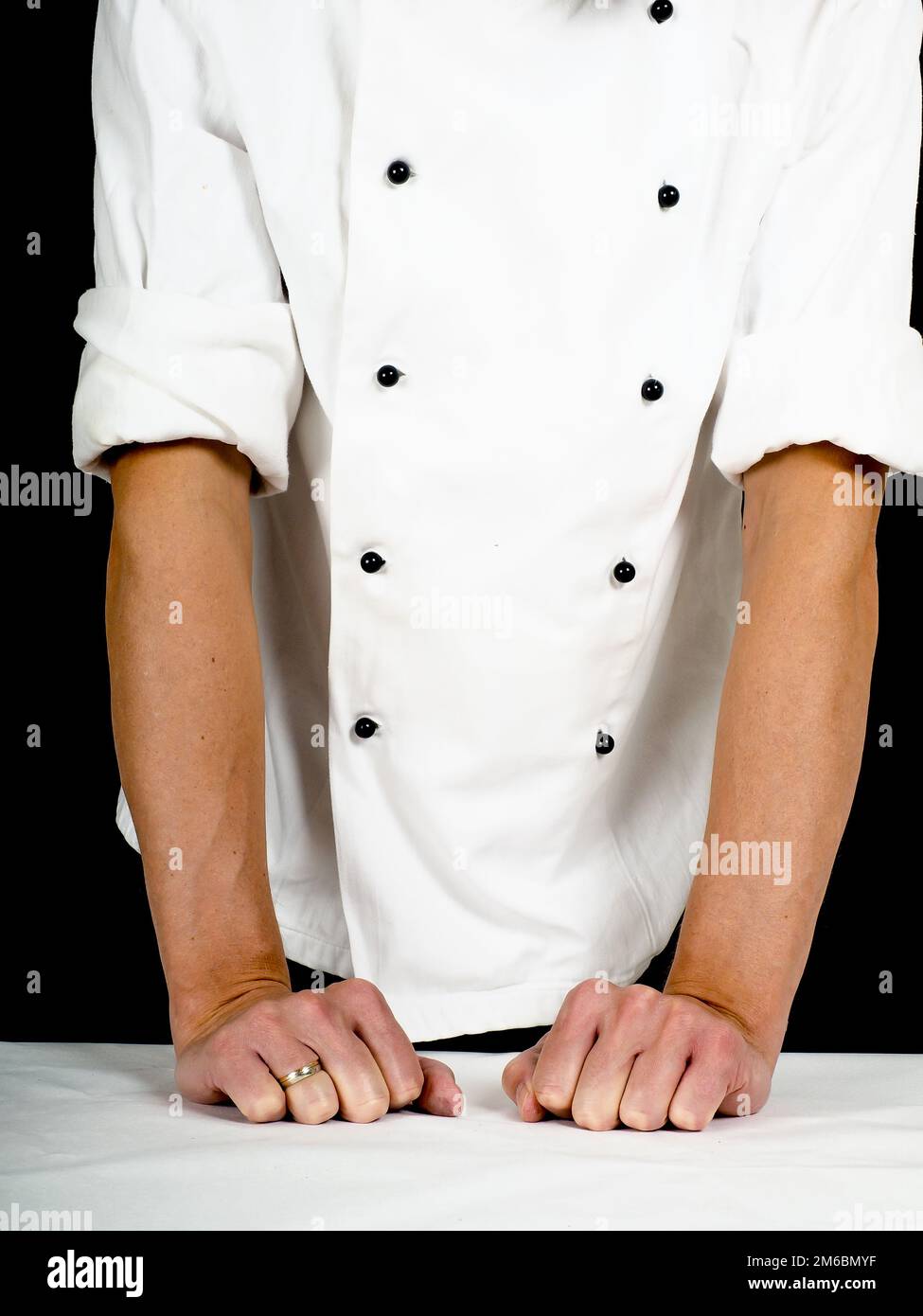 Chef professionnel s'appuyant fermement sur une table avec couvercle blanc Banque D'Images