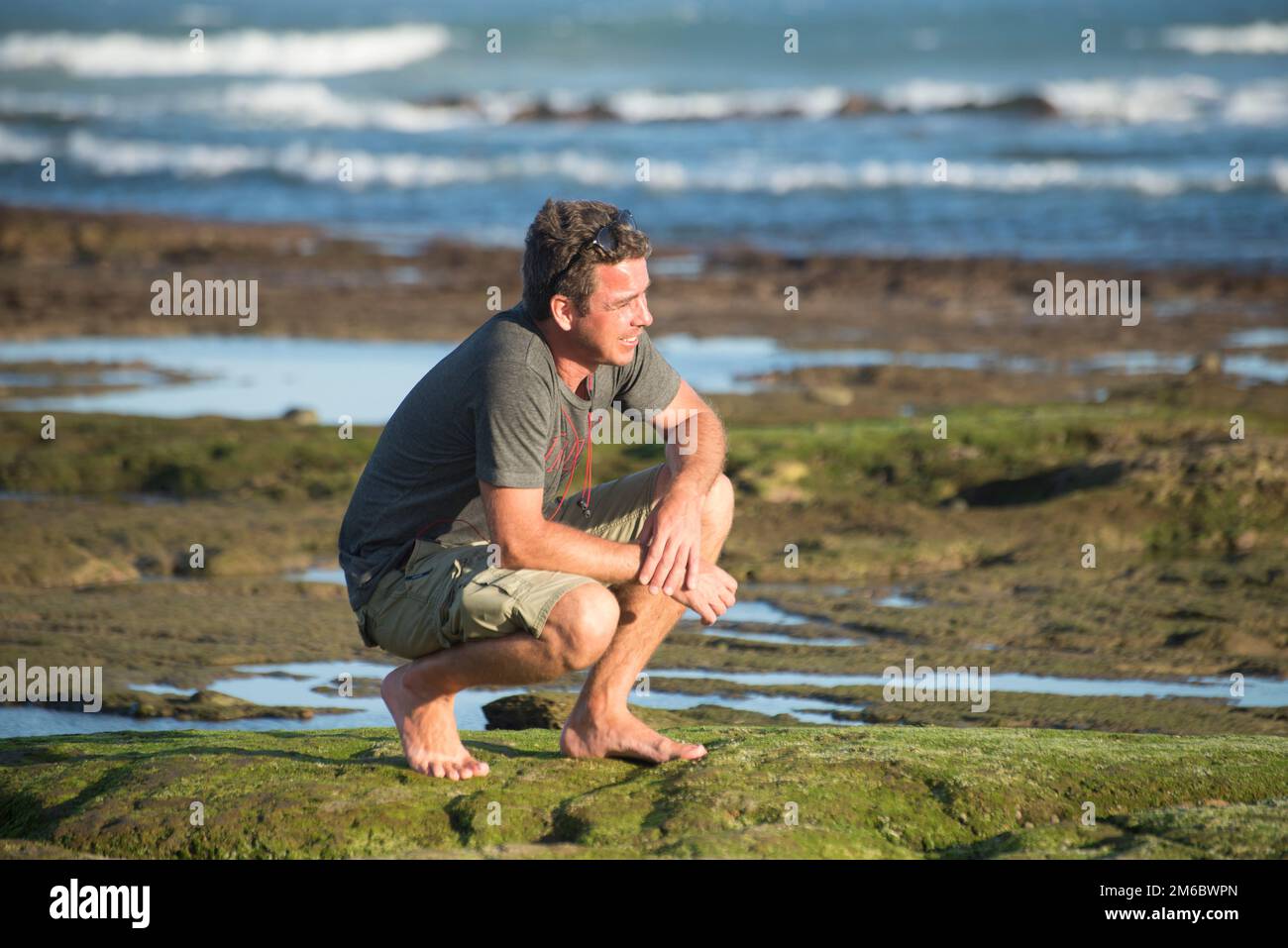L'homme est assis sur ses haunches sur des rochers au bord de l'océan Banque D'Images
