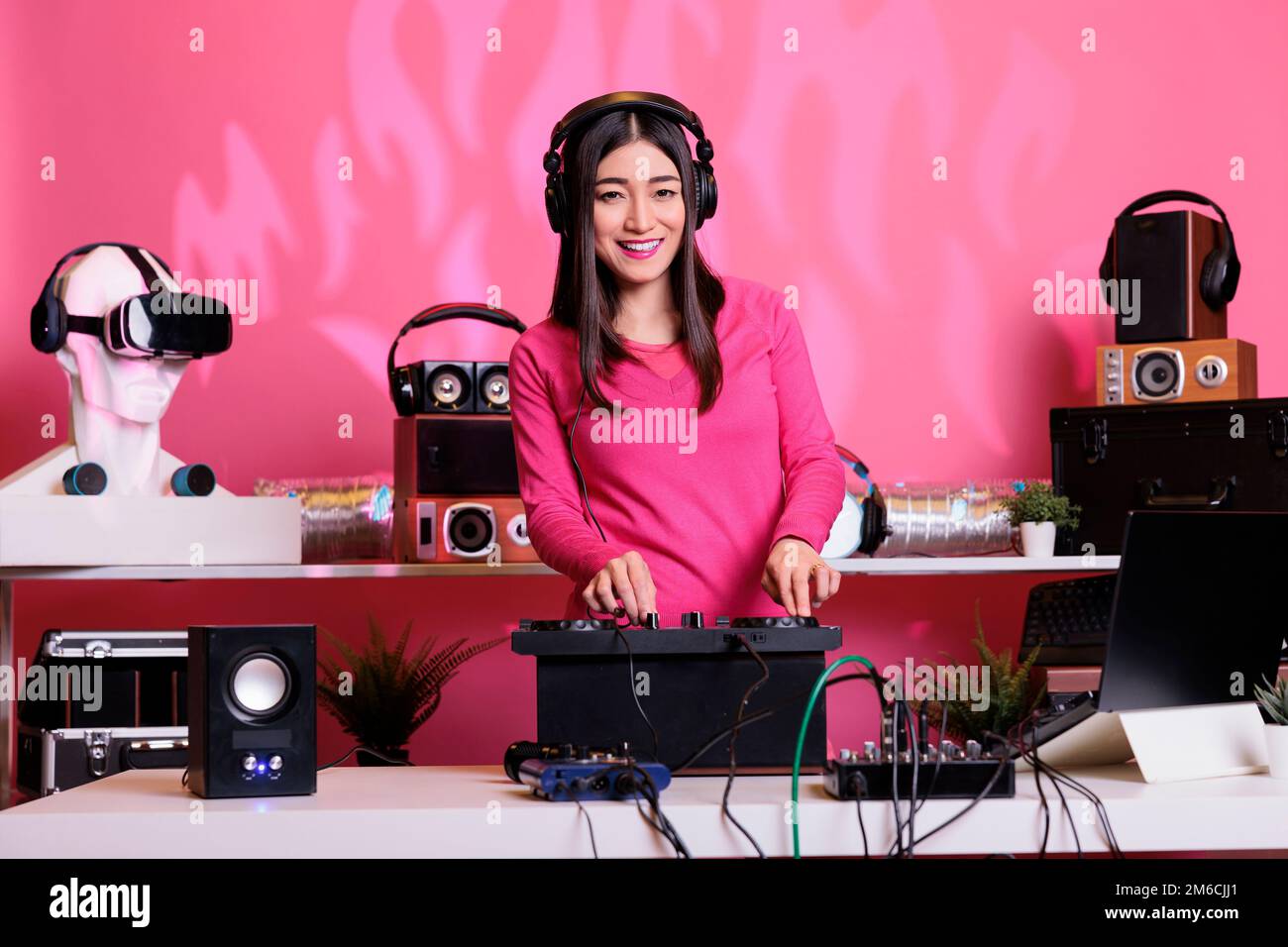 Un musicien asiatique mélange des sons techno électroniques et porte des écouteurs à la table du DJ en club. Représentation en direct à l'aide de platines pour une expérience de concert inoubliable. Entouré de fans à la fête Banque D'Images