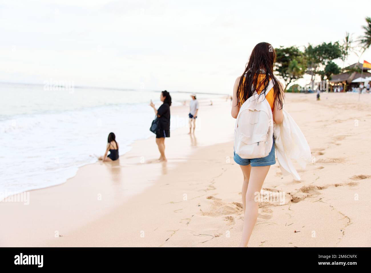 Une jeune femme après avoir nagé dans l'océan avec un sac à dos en vêtements mouillés marche le long de la plage, vacances d'été sur une île près de l'océan à Bali Banque D'Images