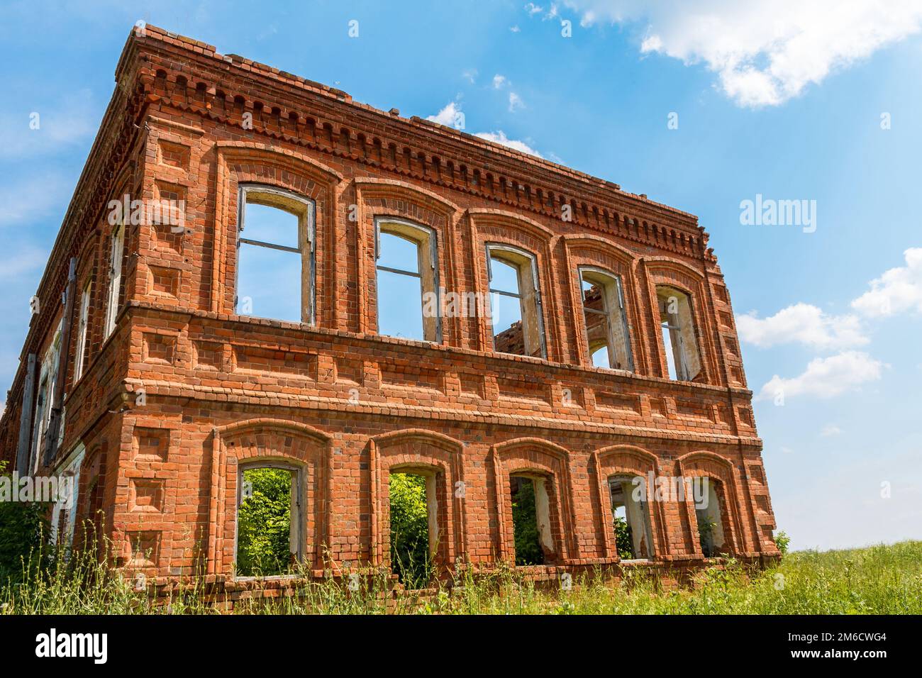 Une grande maison ancienne ruinée de briques rouges contre un ciel bleu avec des nuages blancs. Banque D'Images