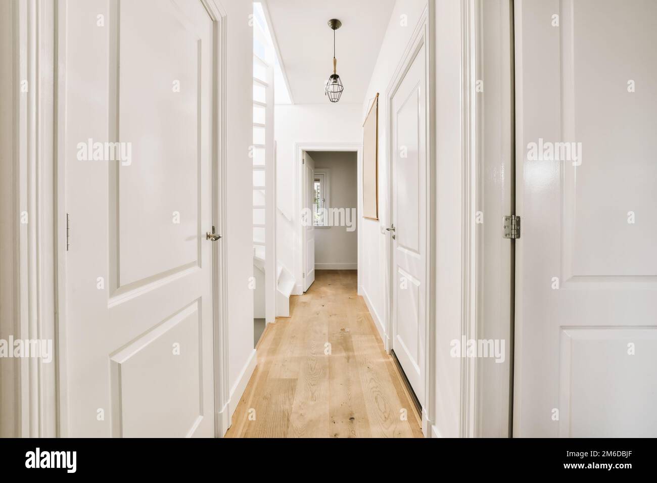 un long couloir avec des murs blancs et du parquet la chambre est bien éclairée par la lumière qui traverse les fenêtres Banque D'Images