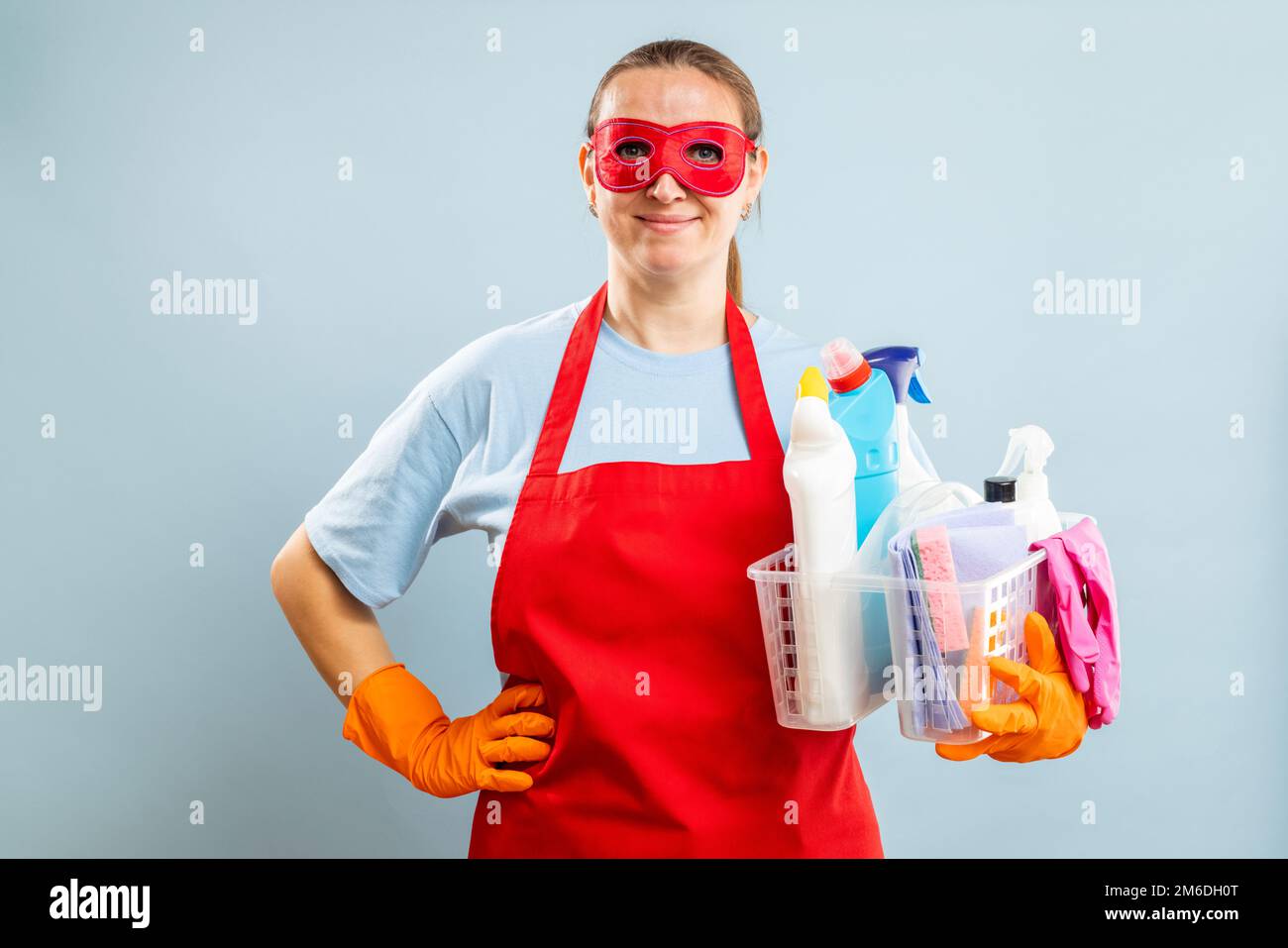 Femme en masque rouge, gants et tablier porte-panier avec fournitures de nettoyage Banque D'Images