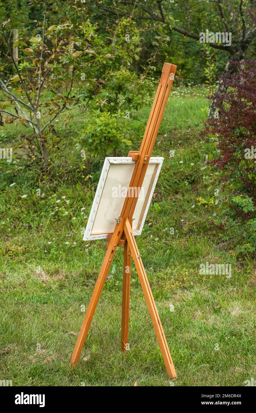 Chevalet de trépied en bois pliable avec cadre en toile prêt pour la  peinture sur l'herbe verte jardin d'été Photo Stock - Alamy