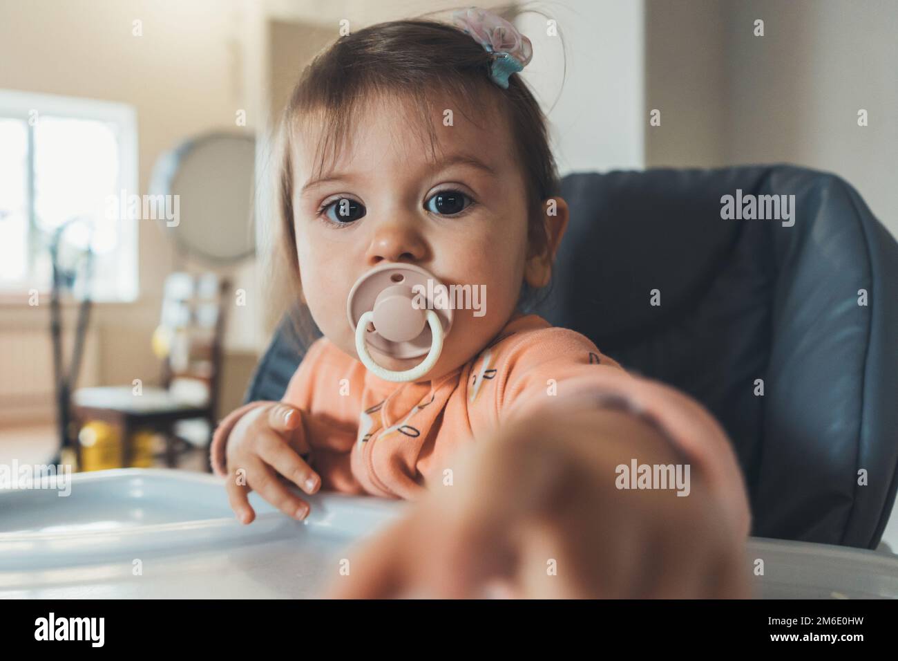 Drôle petite fille caucasienne de bébé assis sur une chaise haute et de jouer avec l'appareil photo. Bonne famille. Visage de beauté. Banque D'Images