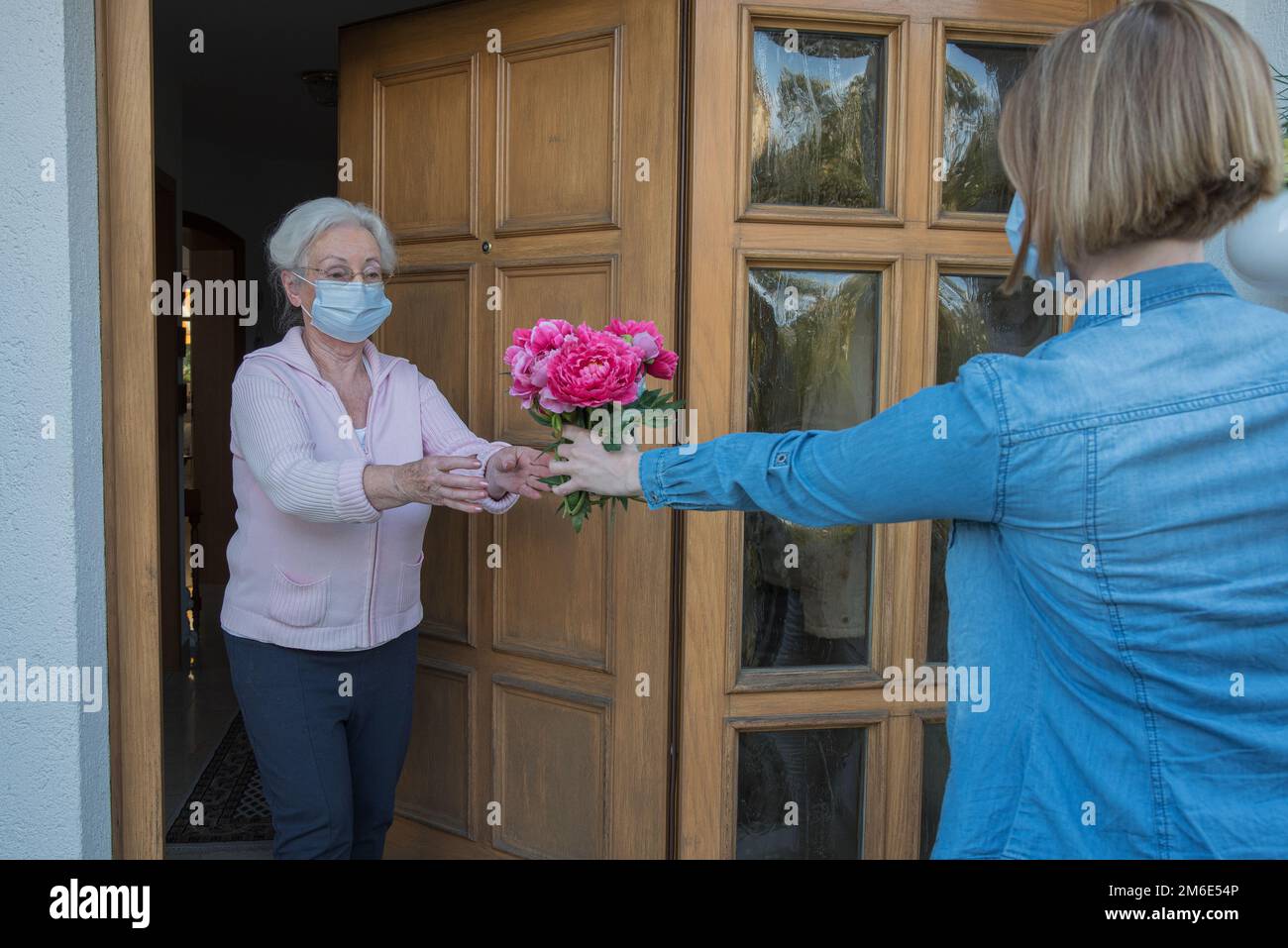 La femme âgée avec masque facial reçoit des fleurs à la porte de la maison de la femme voisine Banque D'Images