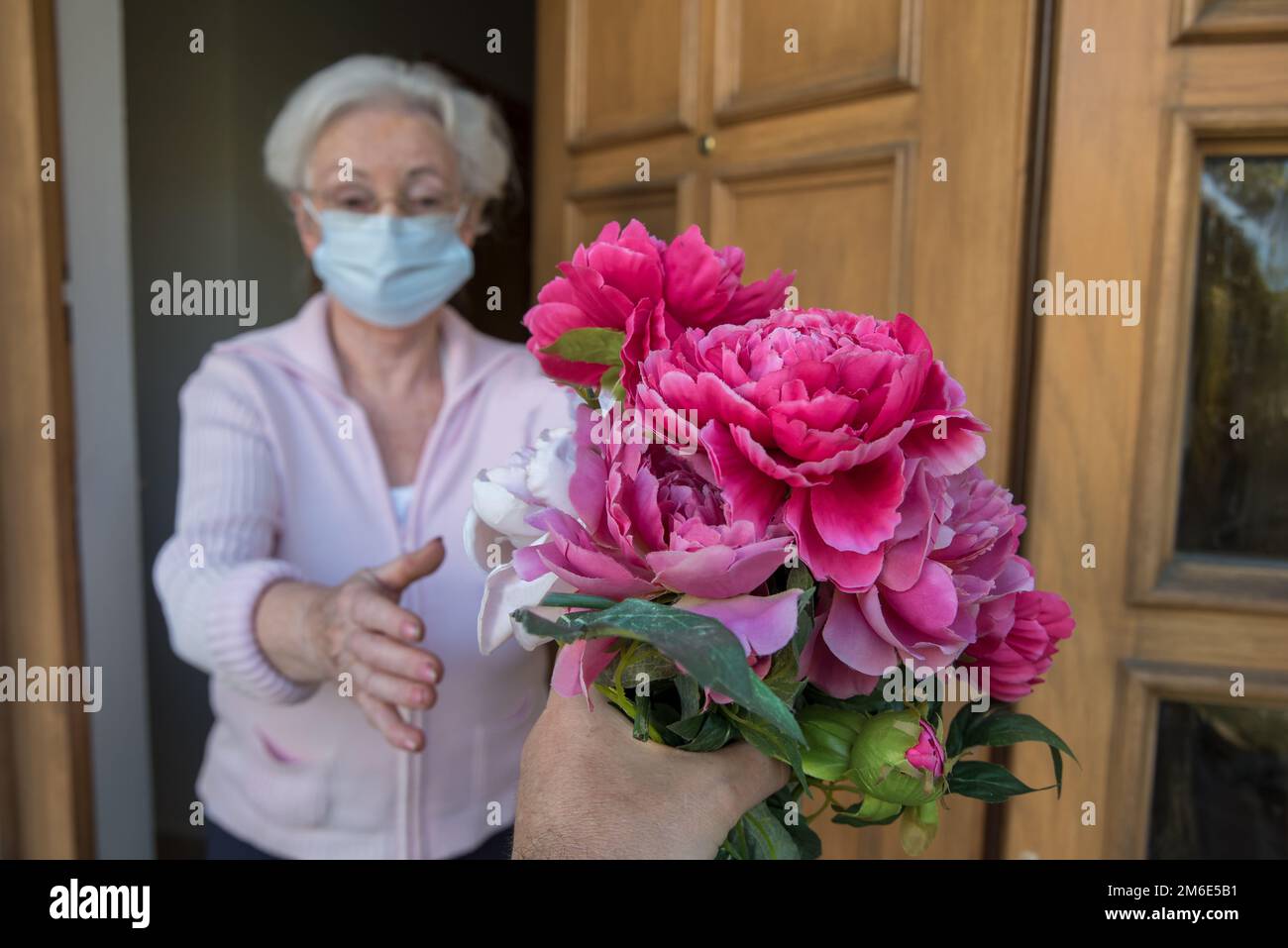 La femme âgée avec masque facial reçoit des fleurs à la porte de la maison Banque D'Images