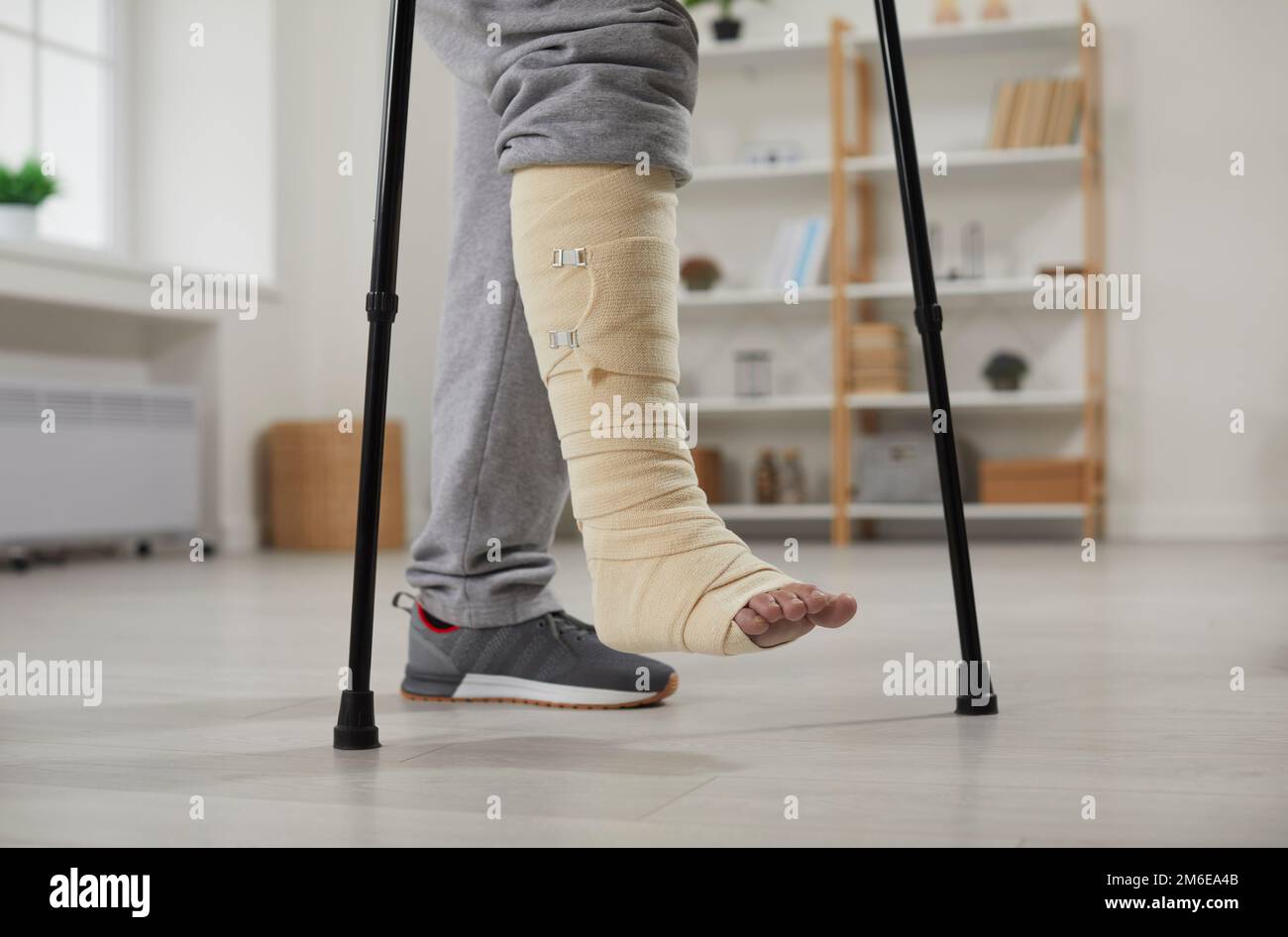 Gros plan des pieds d'un homme avec une cheville cassée dans un bandage marchant avec des béquilles à la maison Banque D'Images
