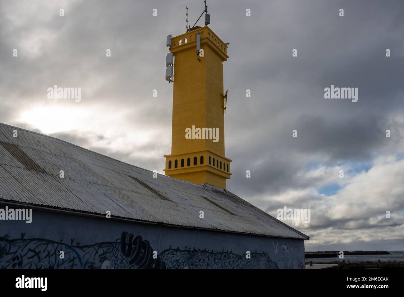 Toit d'un bâtiment et tour peinte en jaune d'un phare simple. Port de Sudurnesjabaer. Ciel nuageux et pluvieux intense. Sudurnesjabaer, Islande. Banque D'Images