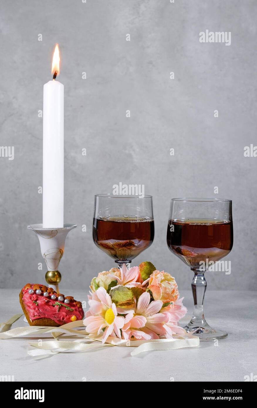 deux verres avec alcool, un bouquet de fleurs et de rubans, une bougie blanche en chandelier sur fond marbré, coeur en pain d'épice, décoration Banque D'Images