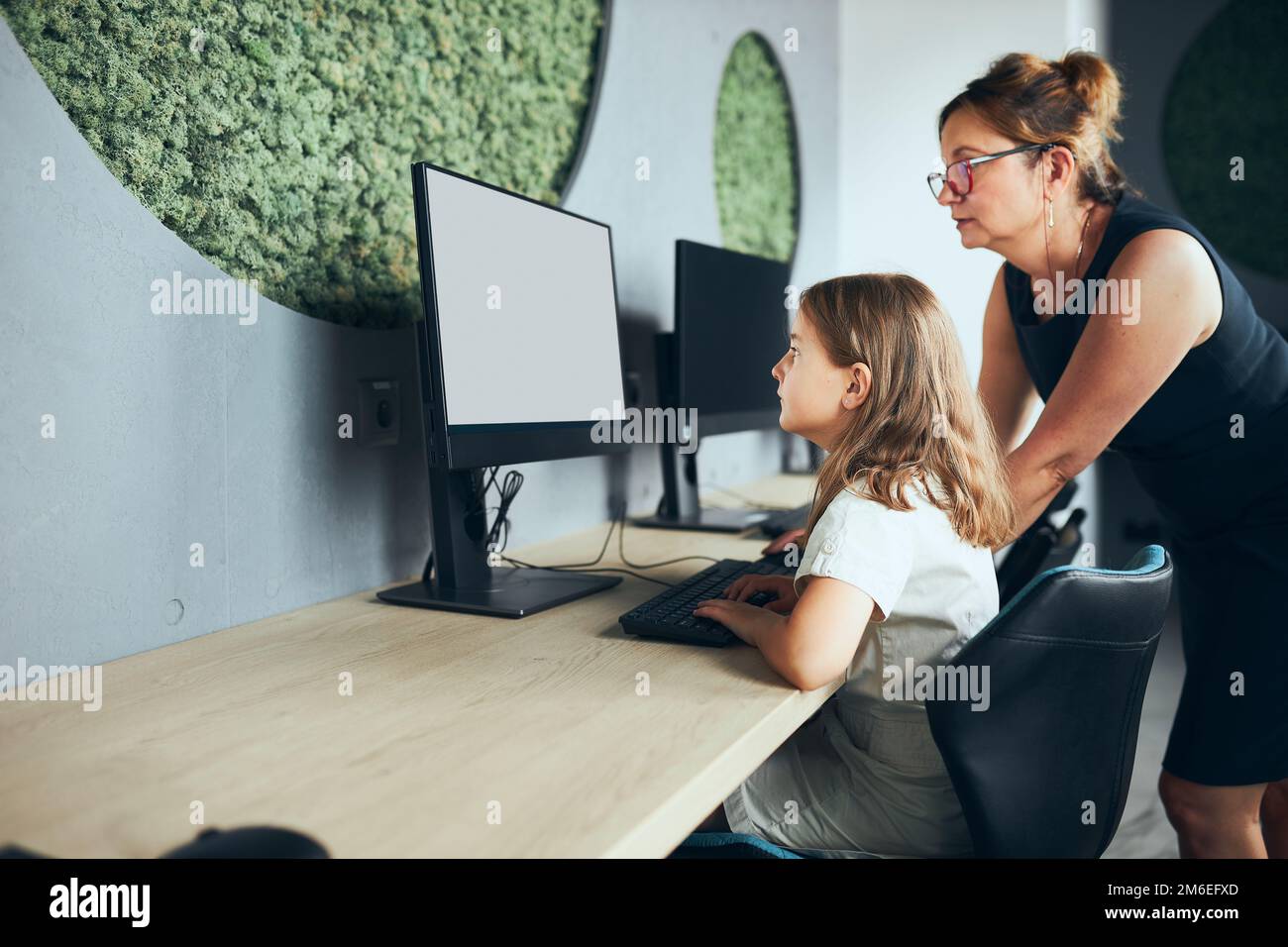 Enseignant aidant une écolière pendant un cours d'informatique à l'école primaire. Ordinateur pour l'apprentissage des enfants en cours élémentaire d'informatique. Enseignant aidant à Banque D'Images