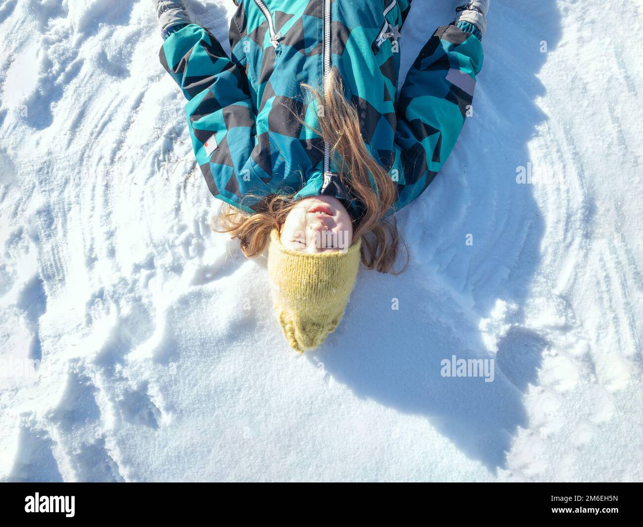 Bonne fille couchée sur la neige et faisant figure d'ange de neige Banque D'Images