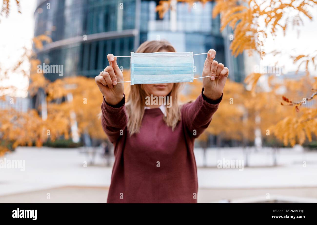 La fille tient un masque médical devant elle. Masque dans les mains d'une femme. Concentrez-vous sur la combinaison. Heure d'automne. Banque D'Images