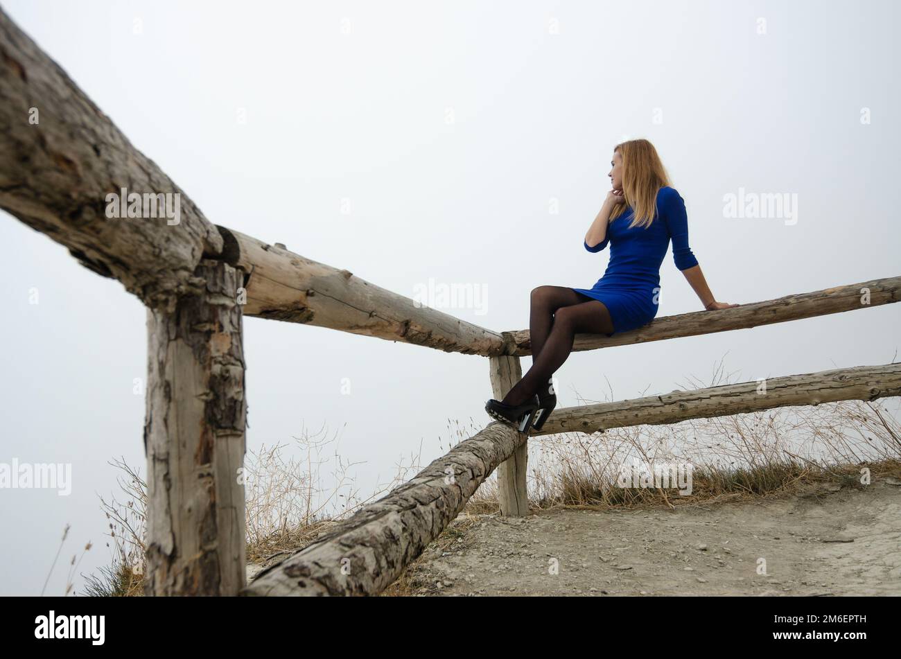 La fille est assise sur une clôture en bois, il y a un brouillard solide autour de la fille Banque D'Images