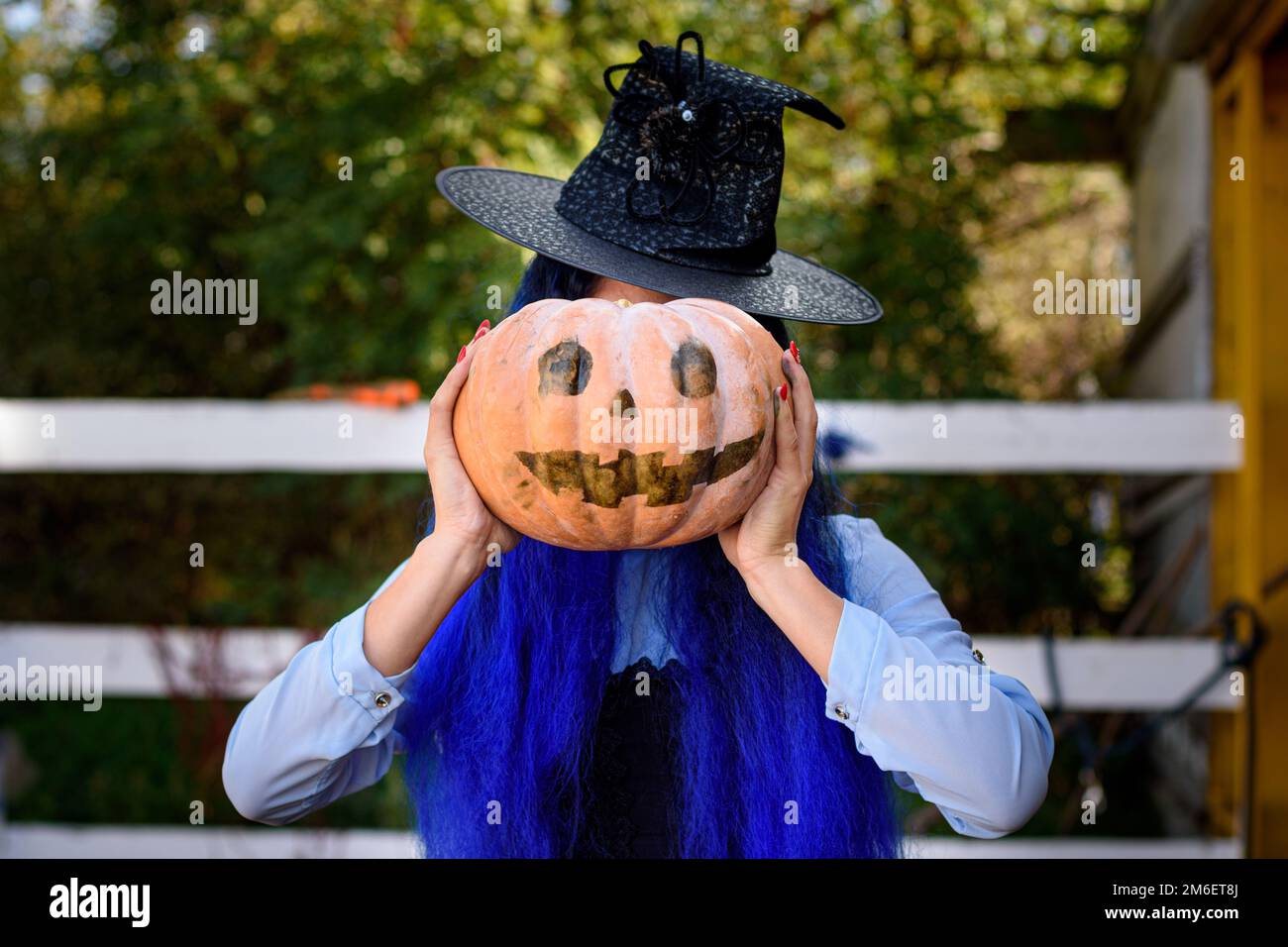 Une fille habillée comme sorcière a couvert son visage avec un potiron avec un visage diabolique dessiné dans le style D'une fête d'Halloween Banque D'Images