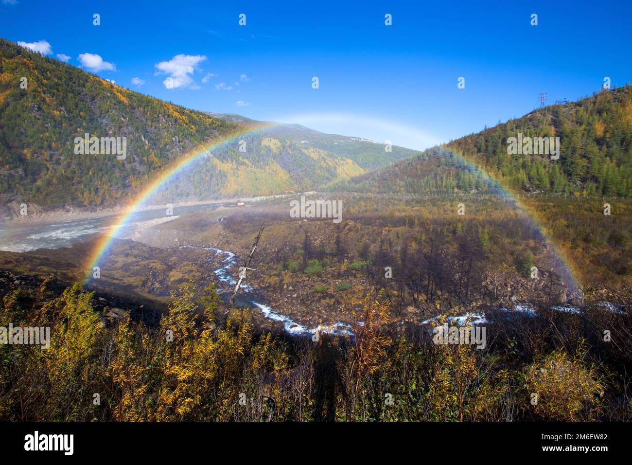 Un bel arc-en-ciel lumineux en pleine taille sur fond de collines d'automne et d'un petit ruisseau. Arc-en-ciel sur l'hydroélectricité d Banque D'Images