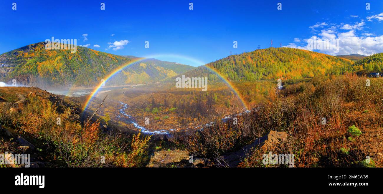 Un bel arc-en-ciel lumineux en pleine taille sur fond de collines d'automne et d'un petit ruisseau. Arc-en-ciel sur l'hydroélectricité d Banque D'Images