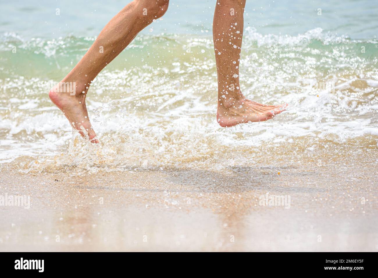 Des pieds drôles qui s'exécutent le long de la plage et qui éclabousse de l'eau Banque D'Images