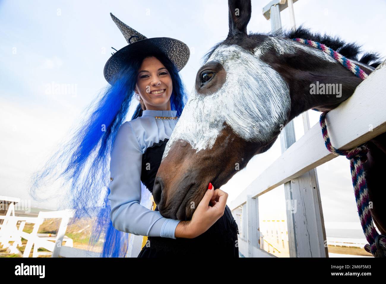 Une fille habillée comme une sorcière se tient à côté d'un cheval sur lequel un squelette est dessiné pour la célébration De Halloween Banque D'Images