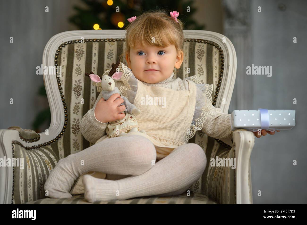 Petite fille drôle ayant le plaisir dans une chaise à l'avant De l'arbre de Noël Banque D'Images
