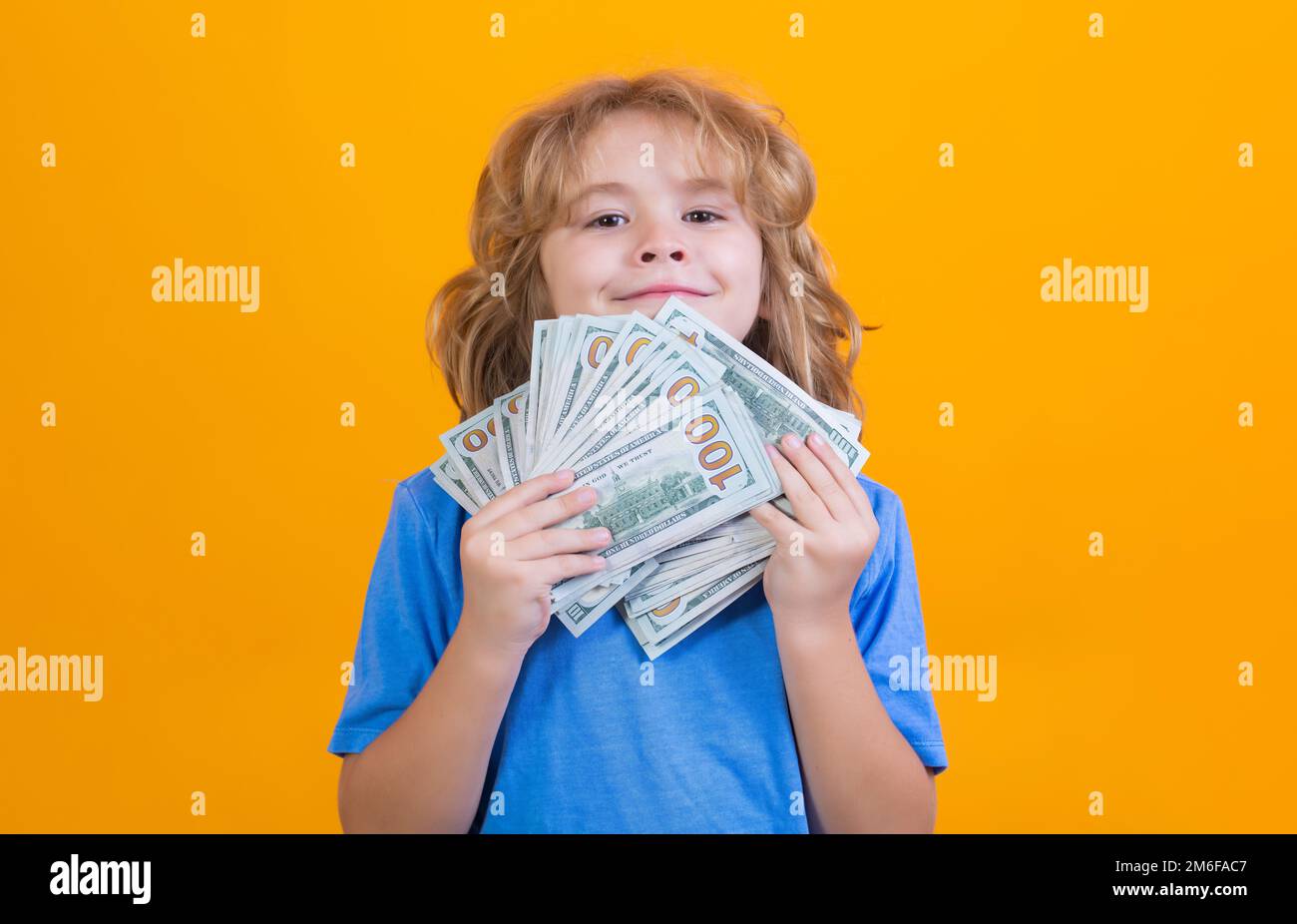Enfant montrant des billets d'argent dollar, debout rêveur de riche contre le fond jaune isolé de studio. Banque D'Images