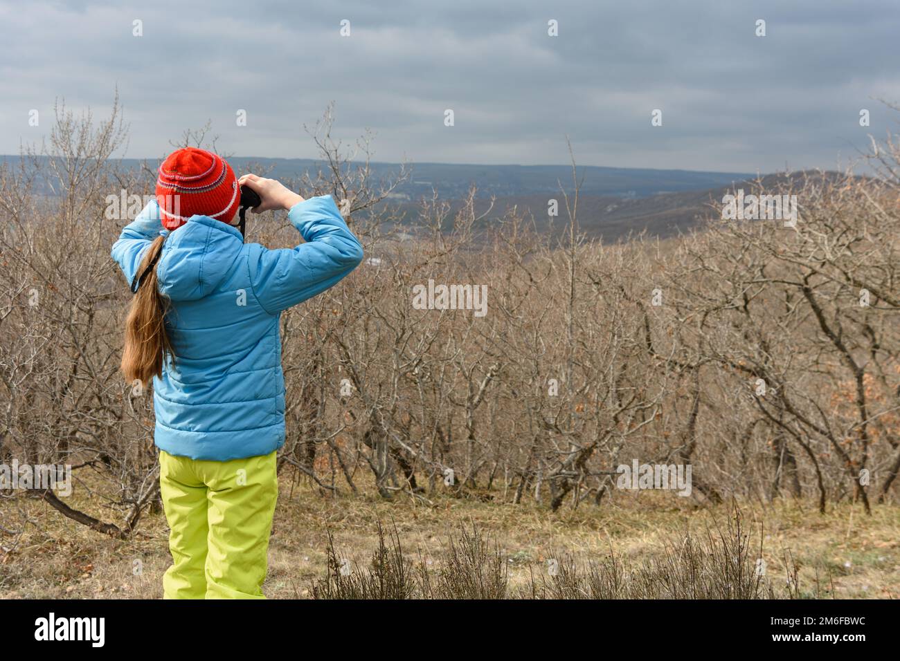 Une fille en automne regarde à travers des jumelles de la montagne, vue arrière Banque D'Images