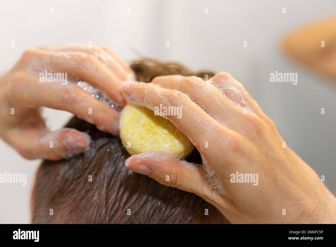 Un homme utilise un bar à shampoing solide dans la salle de bains. Un shampooing d'application sur le cuir chevelu. Soins capillaires durables. Sans plastique, aucun gaspillage, faible niveau d'eau Banque D'Images