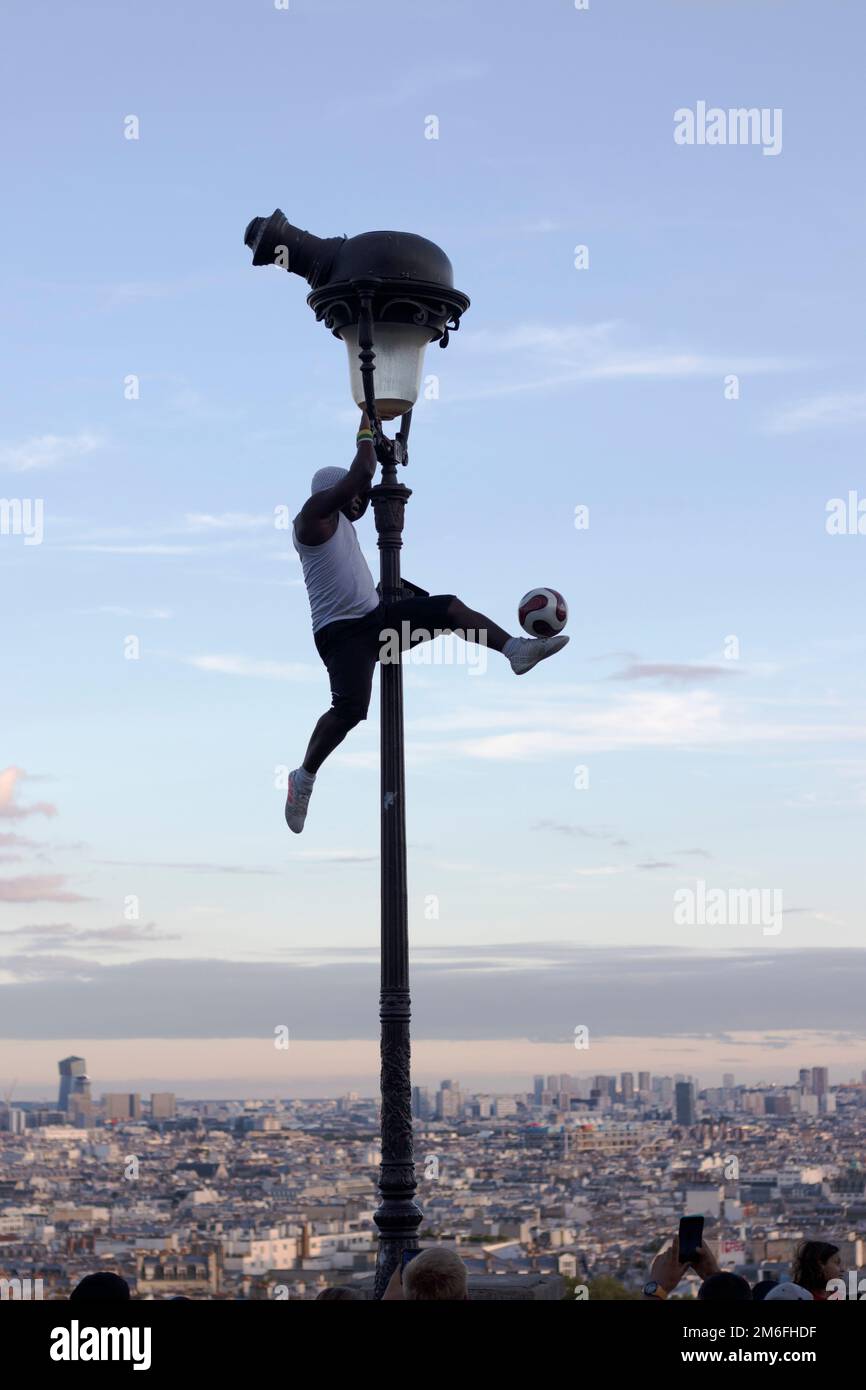 Un artiste de rue à Paris Montmartre monte le lampadaire et frappe une  balle. La ville de Paris est en arrière-plan Photo Stock - Alamy