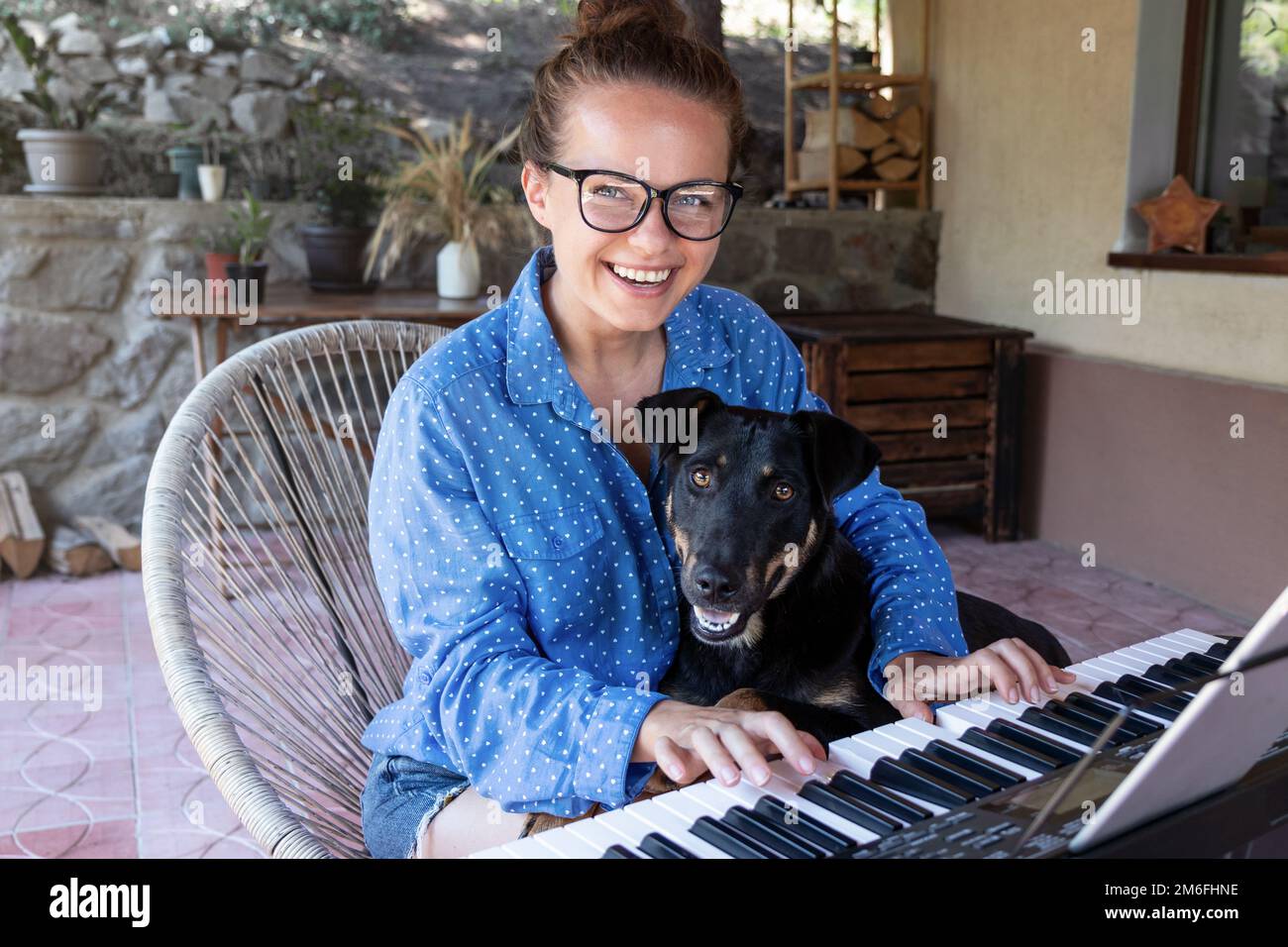Jeune femme en lunettes jouant du piano électrique sur la terrasse avec son chien. Banque D'Images