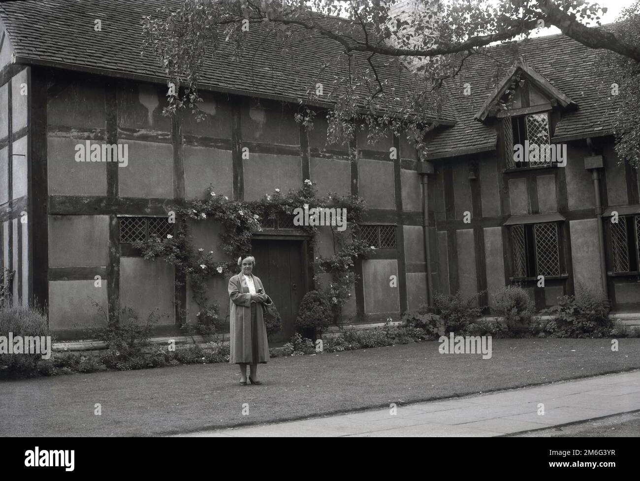 1950s, historique, une dame se tenant sur une pelouse à l'arrière du lieu de naissance de William Shakespeare, une maison à colombages de 16th siècle à Henley Street, Stratford-upon-Avon, Angleterre, Royaume-Uni. La vieille maison a été achetée par le Shakespeare Birthplace Trust en 1847. Banque D'Images