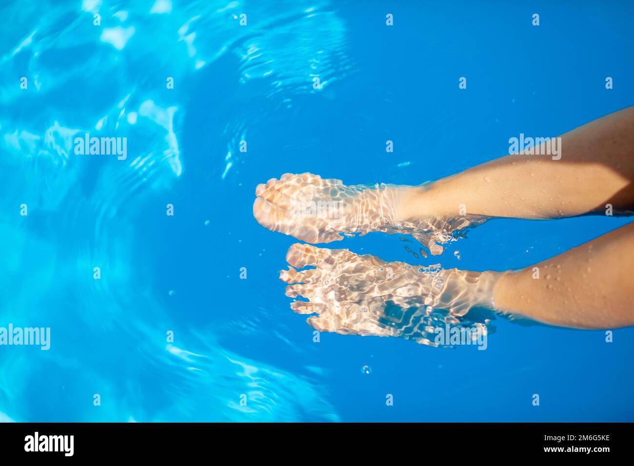 Pattes d'une jeune femme sur le fond de l'eau bleue de la piscine Banque D'Images