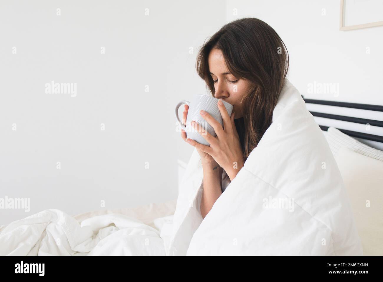 Femme buvant du café dans le lit confortable et confortable Banque D'Images