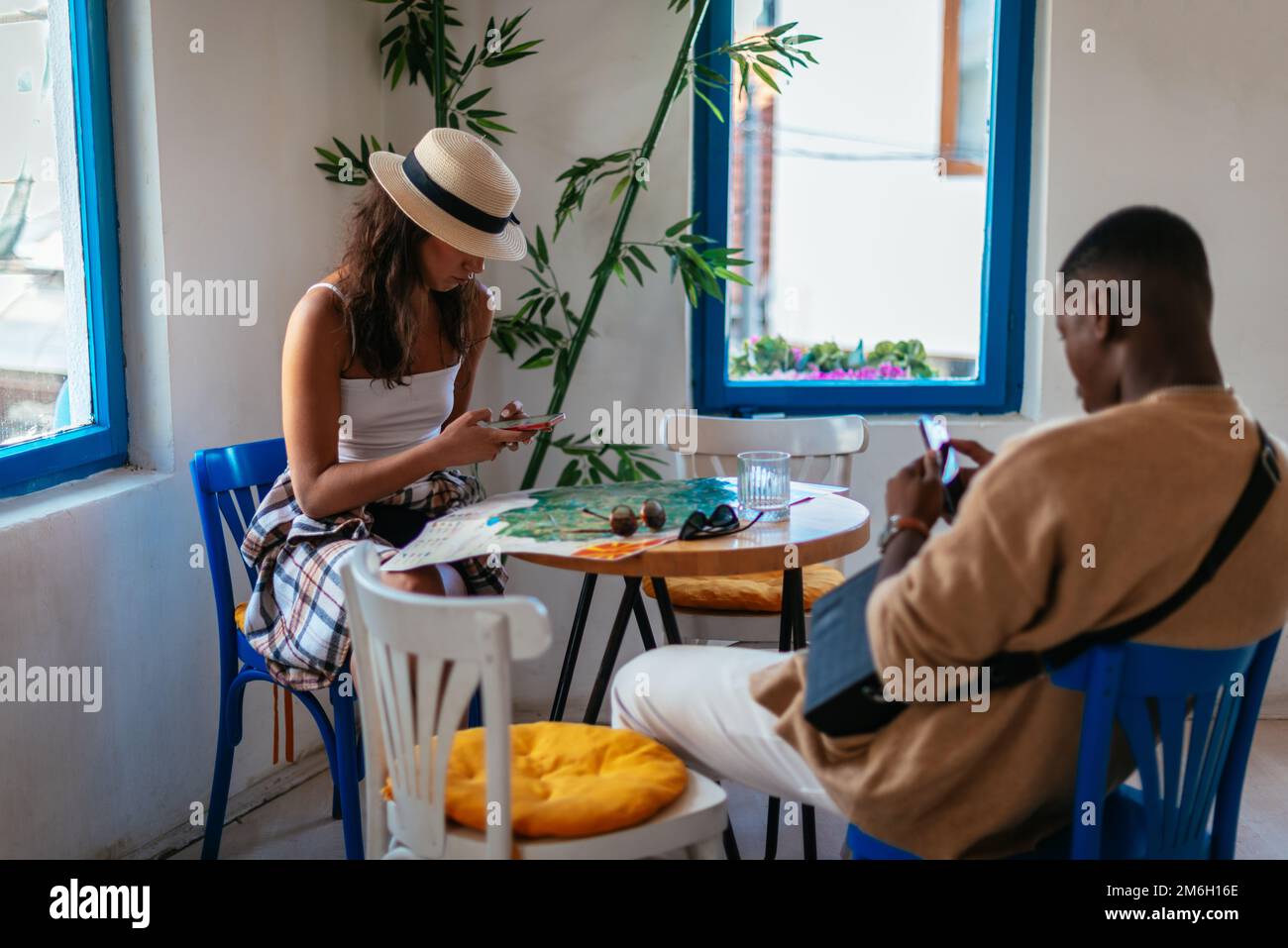 Un homme noir et une femme caucasienne sont assis dans un café. Ils discutent sur leur téléphone Banque D'Images