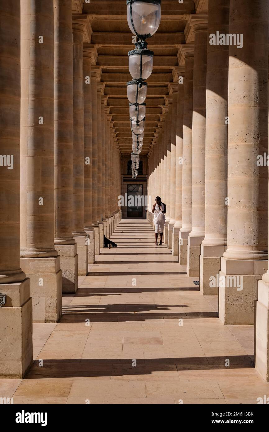 Jeune Noire posant pour des photos dans une robe blanche aux colonnes du Palais Royal à Paris, France - mode, influenceur Banque D'Images