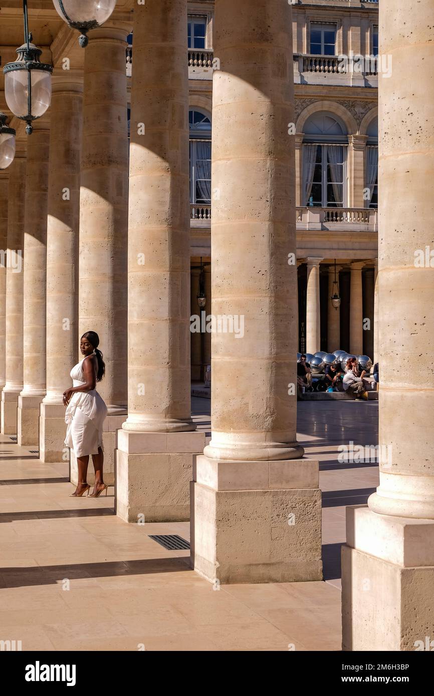 Jeune Noire posant pour des photos dans une robe blanche aux colonnes du Palais Royal à Paris, France - mode, influenceur Banque D'Images