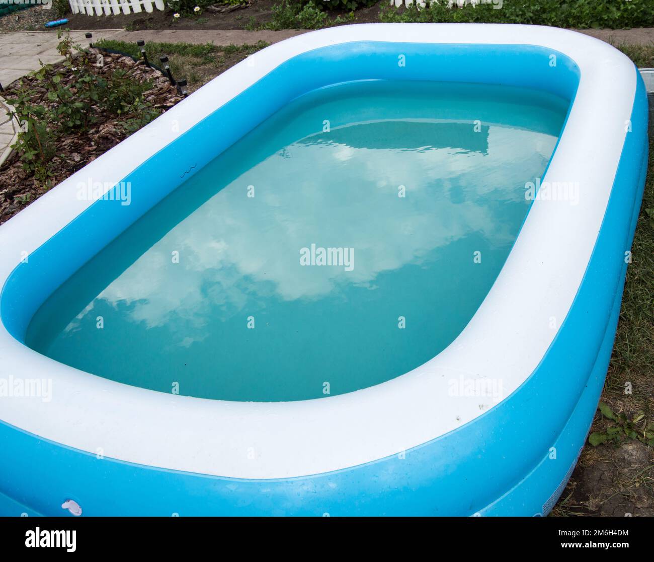 Gros plan d'une piscine gonflable debout sur l'herbe un jour ensoleillé d'été, le reflet des nuages à la surface de l'eau Banque D'Images